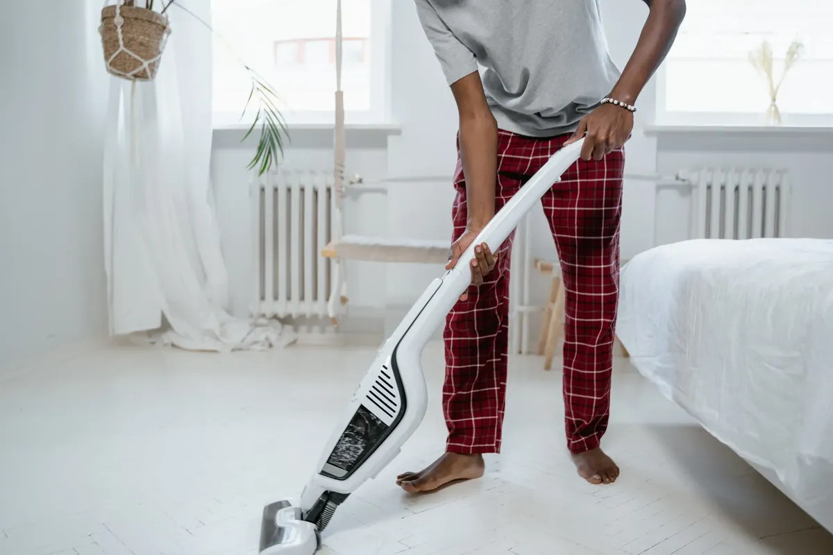 A person cleaning a bedroom with a modern vacuum cleaner, showcasing casual home lifestyle.