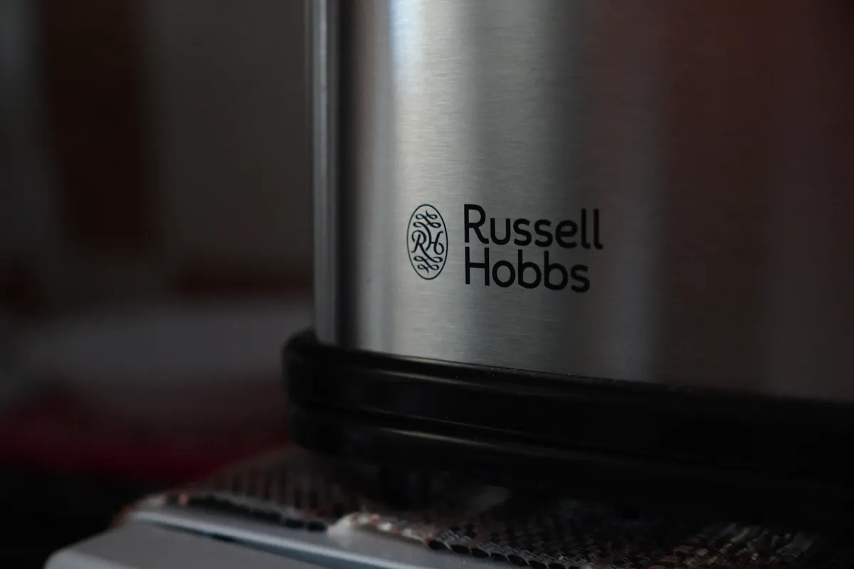 Close-up of the Russell Hobbs logo on a silver appliance with a dark surface in the background.
