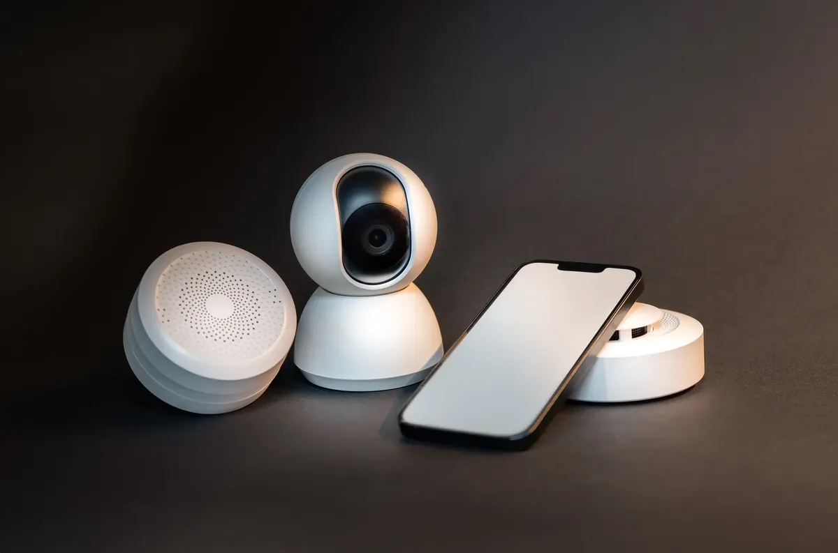 A sleek smartphone with modern smart home devices on a minimalist gray background.