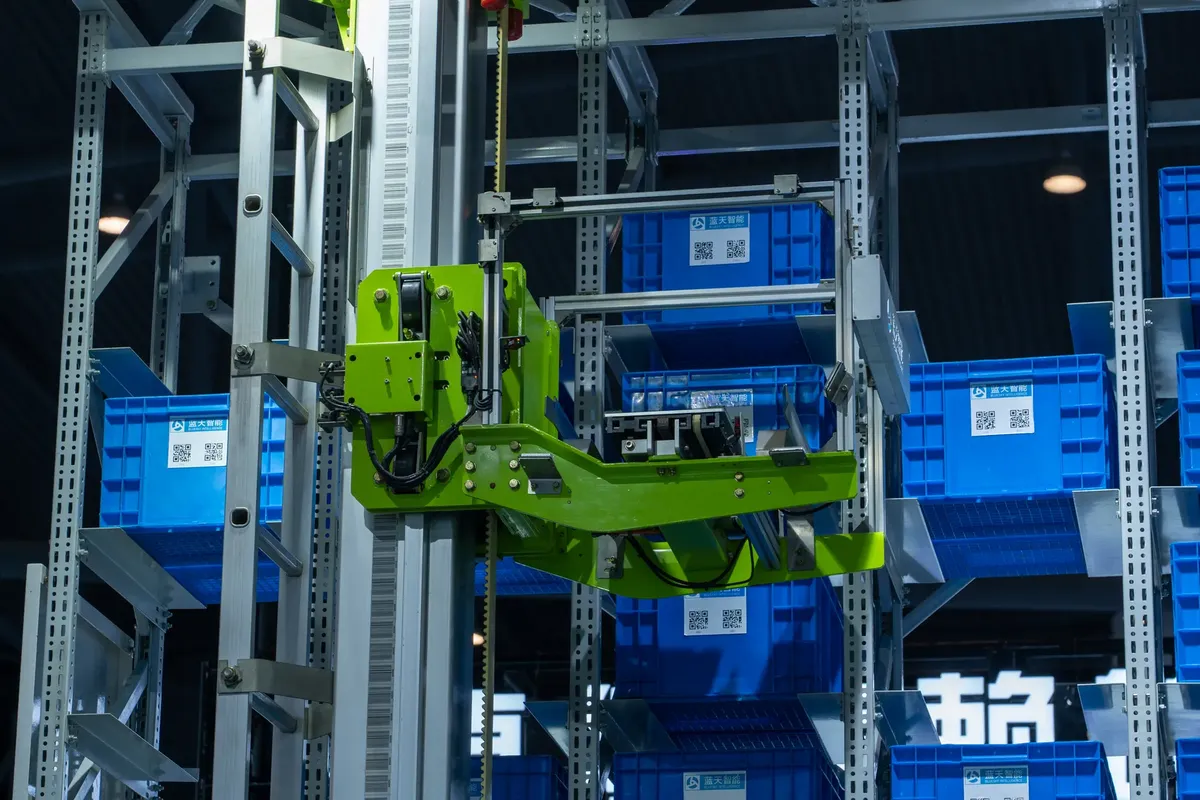 高技術の自動化された倉庫システムで、青い保管箱を処理している緑色のロボットアームが含まれている。