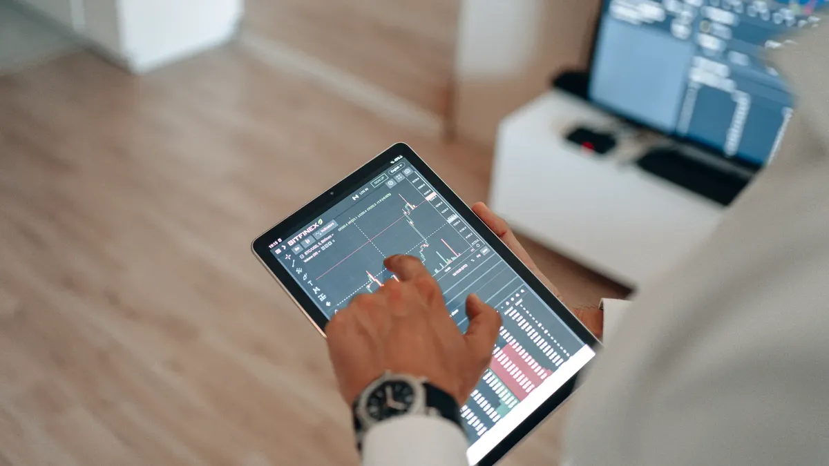 A person holding a tablet indoors displaying financial trading graphs, engaging in digital finance analysis.