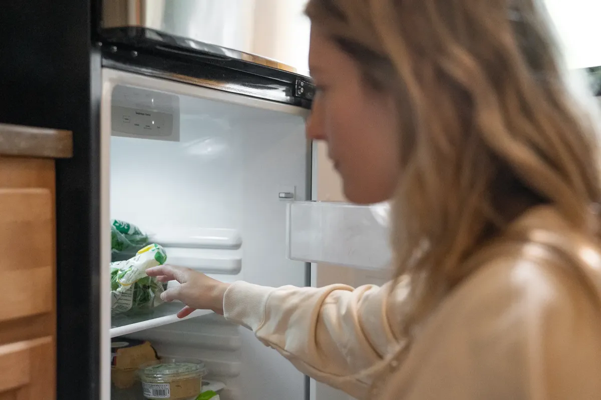 Woman grabbing vegetables from a refrigerator, symbolizing healthy living.